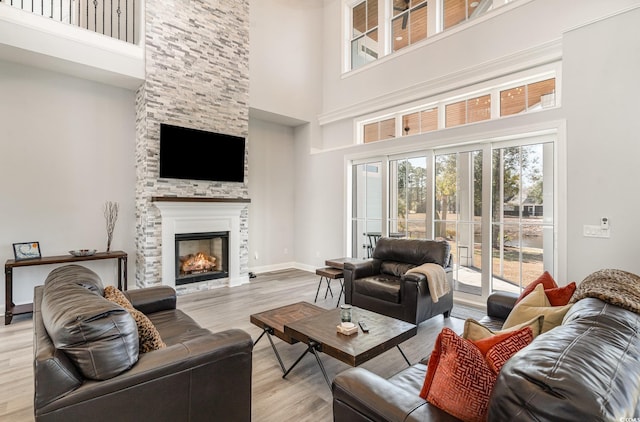 living room featuring light wood-type flooring, a high ceiling, baseboards, and a stone fireplace