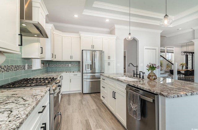 kitchen featuring a raised ceiling, stainless steel appliances, wall chimney range hood, and a sink