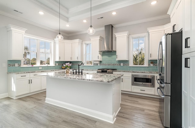 kitchen with a center island, visible vents, appliances with stainless steel finishes, white cabinets, and wall chimney range hood