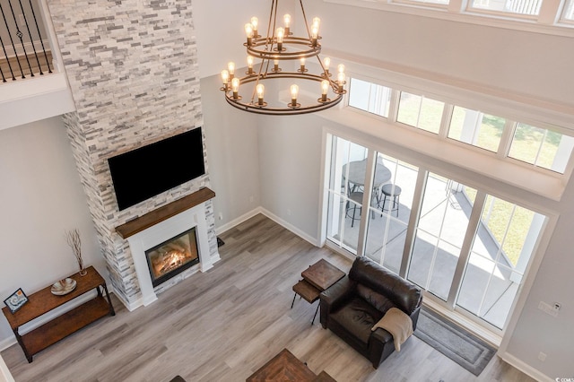 living area featuring light wood-type flooring, a fireplace, a high ceiling, and a chandelier