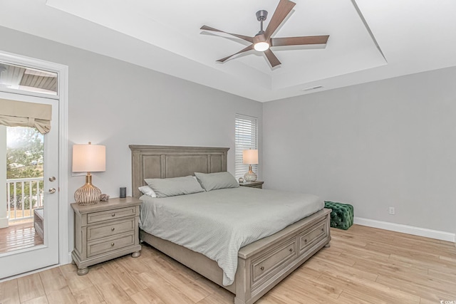 bedroom featuring a raised ceiling, access to exterior, light wood-type flooring, baseboards, and a ceiling fan