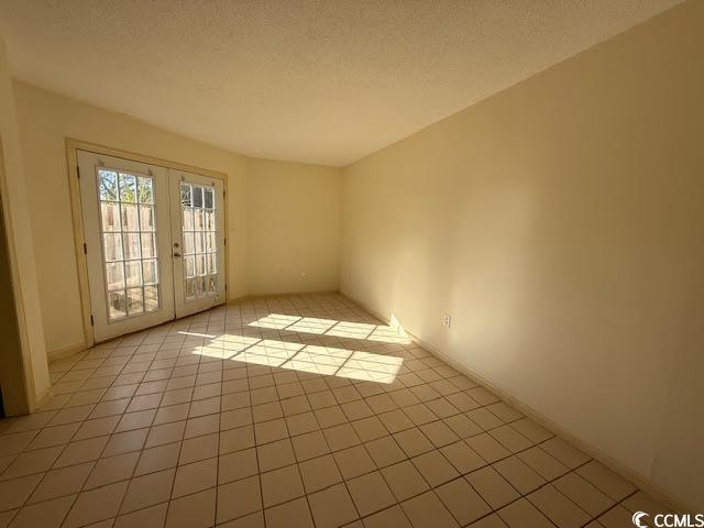 empty room with a textured ceiling, french doors, and light tile patterned floors