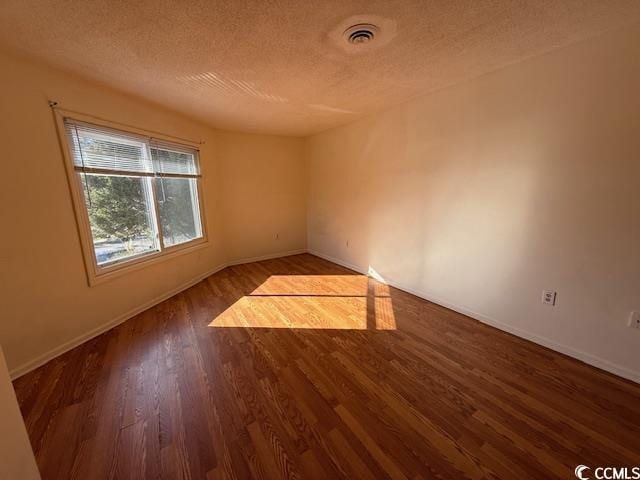 spare room featuring baseboards, a textured ceiling, visible vents, and wood finished floors