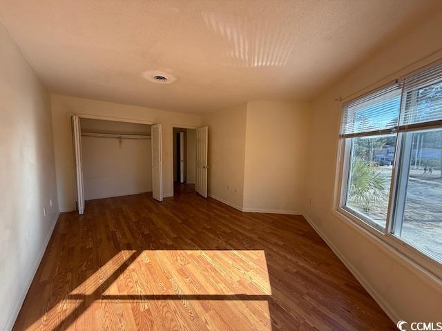 unfurnished bedroom with a closet, baseboards, and dark wood-type flooring