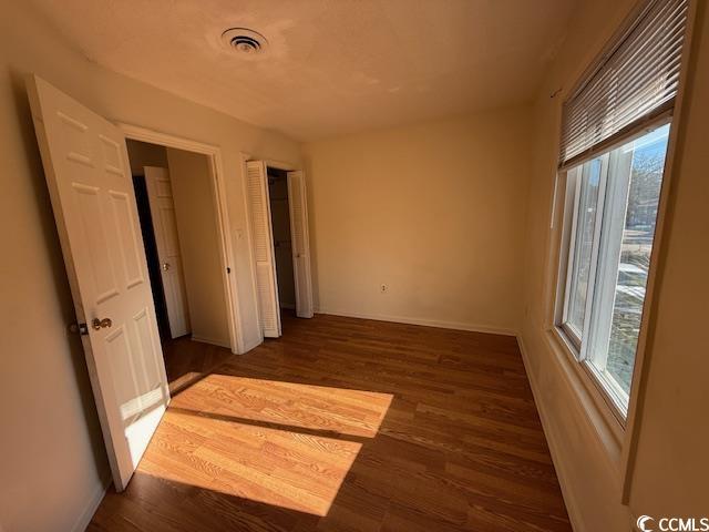 empty room featuring visible vents, dark wood finished floors, and baseboards