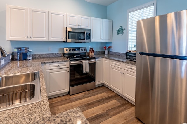 kitchen with appliances with stainless steel finishes, light wood-style floors, white cabinetry, a sink, and light stone countertops