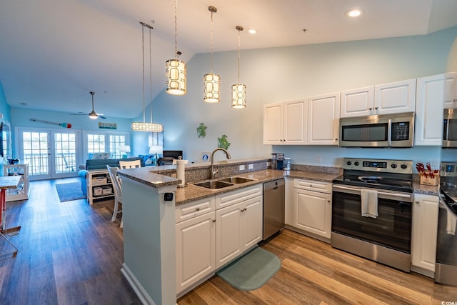 kitchen with stainless steel appliances, white cabinetry, a sink, and decorative light fixtures