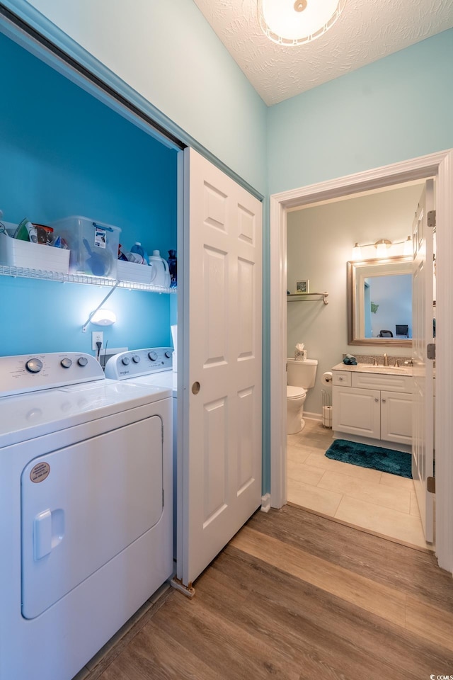 washroom with wood finished floors, a sink, a textured ceiling, separate washer and dryer, and laundry area