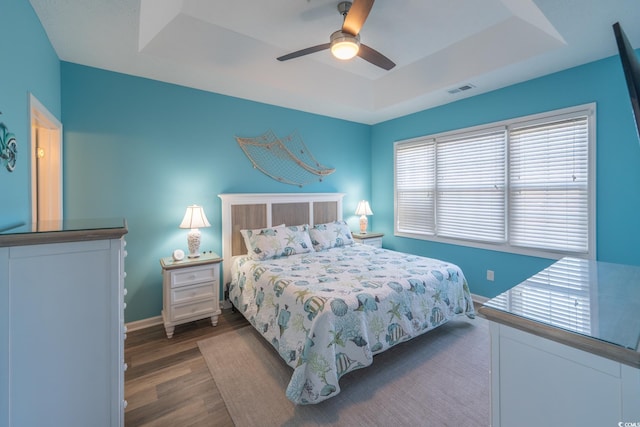 bedroom with a tray ceiling, dark wood-style flooring, visible vents, and baseboards