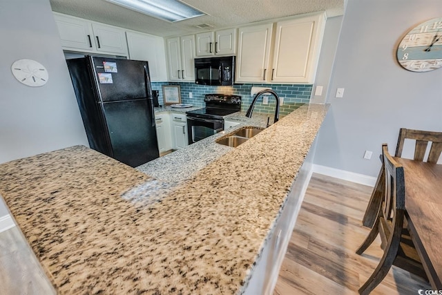 kitchen featuring light stone counters, backsplash, a sink, a peninsula, and black appliances