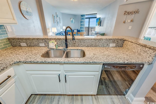 kitchen featuring black dishwasher, light stone counters, white cabinets, and a sink