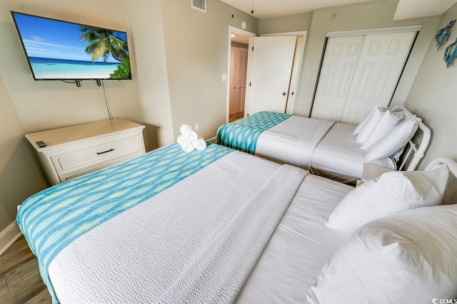 bedroom with a closet, wood finished floors, visible vents, and baseboards