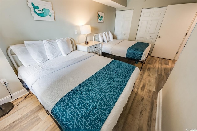 bedroom featuring two closets, baseboards, and wood finished floors