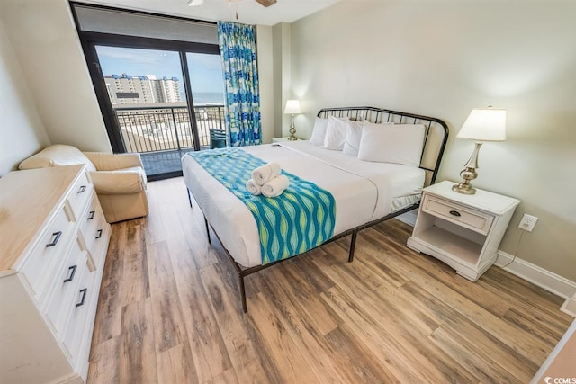 bedroom featuring access to outside, a city view, light wood-style flooring, and baseboards