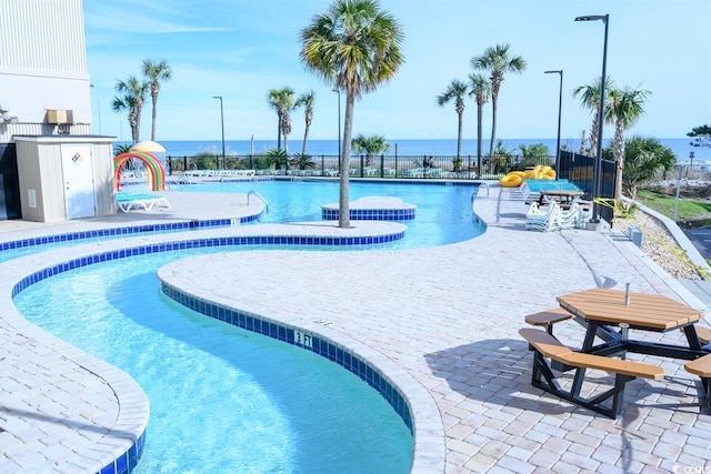 pool with a water view, fence, and a patio