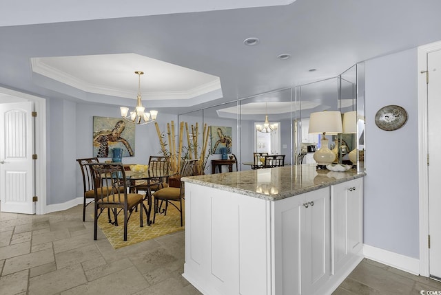 kitchen featuring decorative light fixtures, a notable chandelier, a raised ceiling, white cabinetry, and dark stone counters