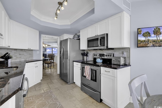 kitchen with stone tile floors, white cabinets, a raised ceiling, dark stone counters, and appliances with stainless steel finishes