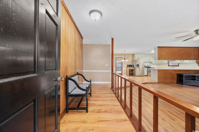 hall featuring light wood-type flooring, a sink, a textured ceiling, and baseboards