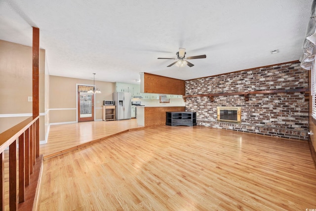 unfurnished living room featuring light wood-style floors, a textured ceiling, brick wall, baseboards, and ceiling fan with notable chandelier