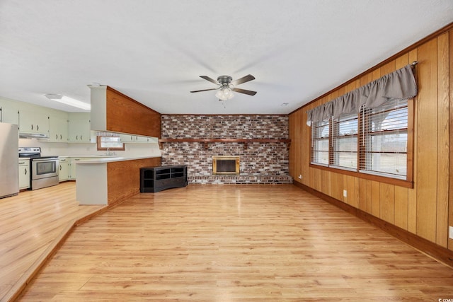 unfurnished living room with light wood-type flooring, ceiling fan, wooden walls, and a textured ceiling