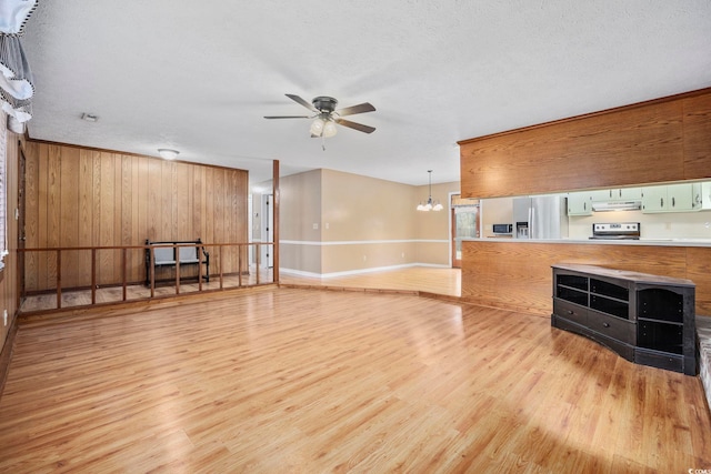 unfurnished living room with ceiling fan with notable chandelier, light wood finished floors, a textured ceiling, and baseboards