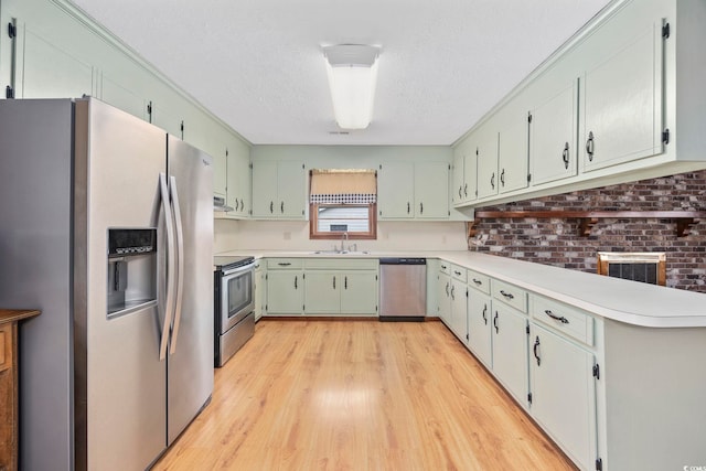 kitchen with stainless steel appliances, light countertops, a sink, a textured ceiling, and light wood-type flooring