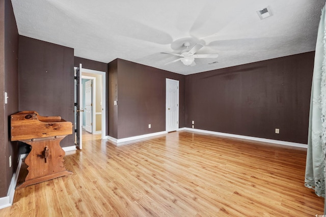 spare room featuring light wood finished floors, baseboards, visible vents, and a ceiling fan