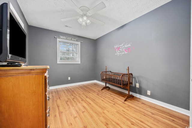 bedroom featuring light wood finished floors, baseboards, visible vents, and a textured ceiling