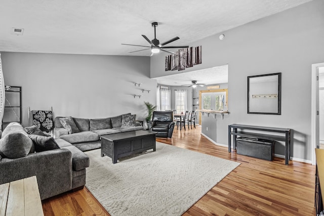 living area featuring lofted ceiling, visible vents, baseboards, and wood finished floors