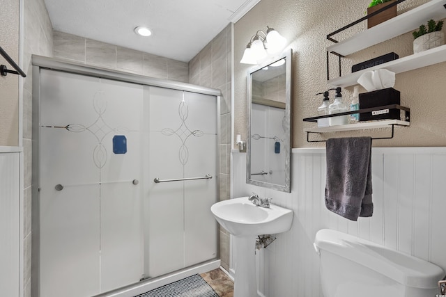 bathroom with toilet, a wainscoted wall, a shower stall, and a textured wall