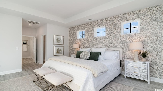 bedroom featuring baseboards, visible vents, wood finished floors, and wallpapered walls