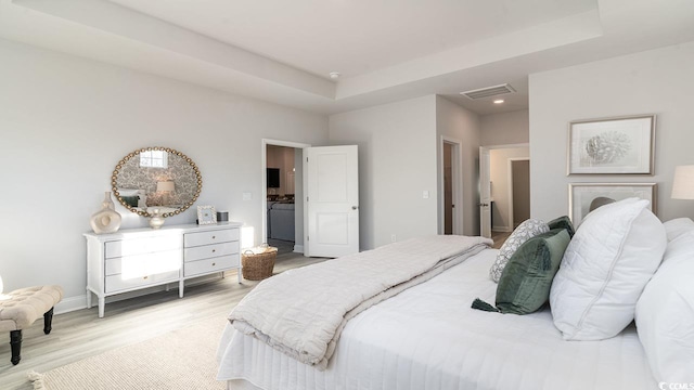 bedroom with a raised ceiling, baseboards, light wood-style floors, and visible vents