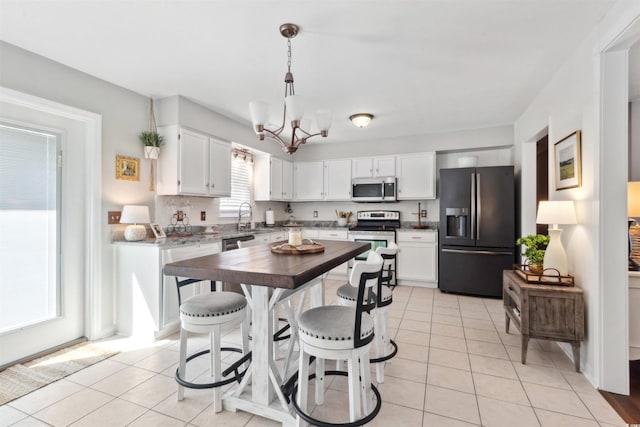 kitchen with hanging light fixtures, light tile patterned floors, appliances with stainless steel finishes, and white cabinets