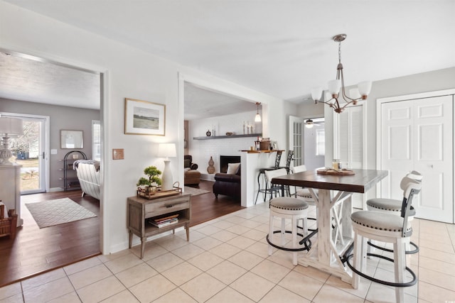 dining space featuring baseboards, a fireplace, an inviting chandelier, and light tile patterned floors