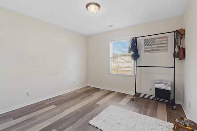 empty room featuring wood finished floors, visible vents, and baseboards