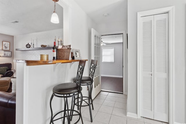 kitchen featuring light tile patterned floors, baseboards, visible vents, a kitchen breakfast bar, and decorative light fixtures