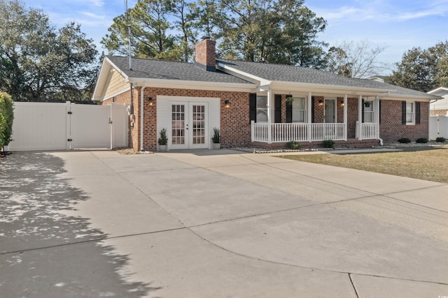 ranch-style house with covered porch, brick siding, french doors, a gate, and a chimney