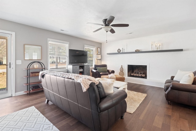 living area with a brick fireplace, dark wood-style flooring, ceiling fan, and baseboards