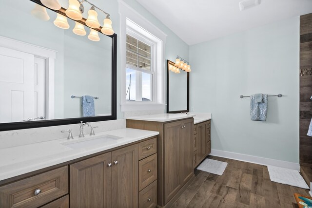 full bathroom featuring wood finished floors, two vanities, a sink, and baseboards
