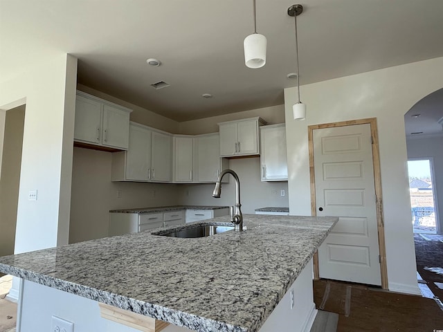 kitchen featuring visible vents, a sink, an island with sink, and light stone countertops