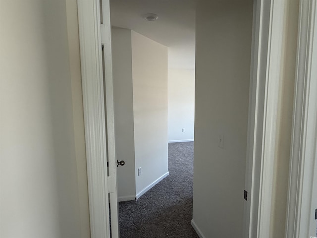 hallway featuring dark carpet and baseboards