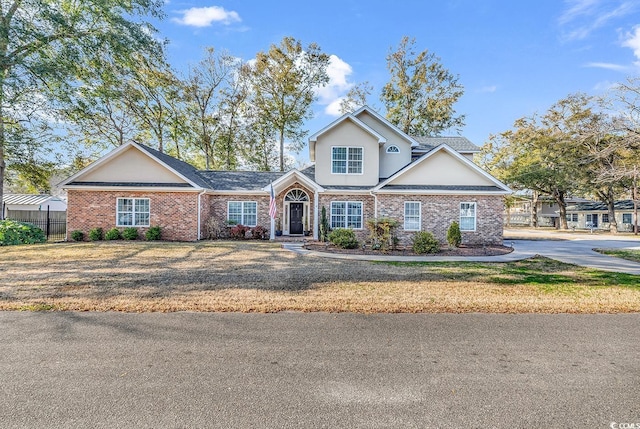 traditional-style house with brick siding, a front yard, fence, and stucco siding