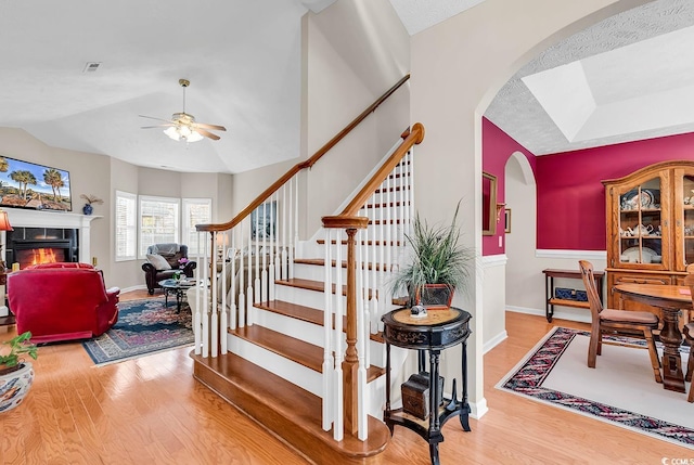 staircase with a ceiling fan, a tile fireplace, arched walkways, and wood finished floors