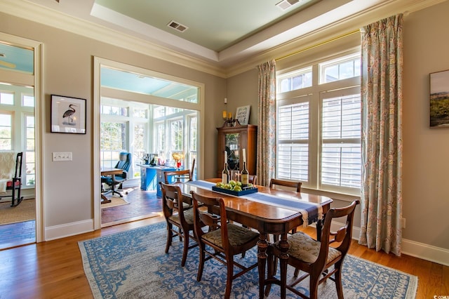 dining area with visible vents, baseboards, a raised ceiling, wood finished floors, and crown molding