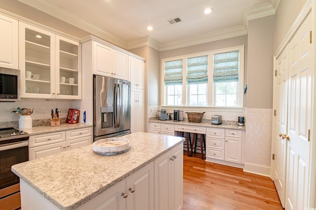 kitchen featuring light wood finished floors, appliances with stainless steel finishes, glass insert cabinets, ornamental molding, and a kitchen island