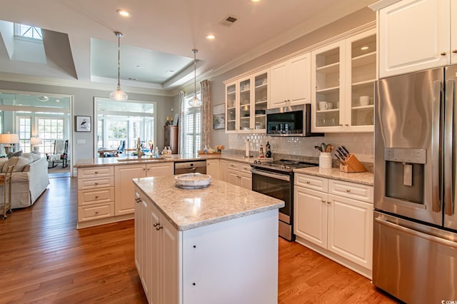 kitchen with a center island, a peninsula, a tray ceiling, stainless steel appliances, and light wood-style floors