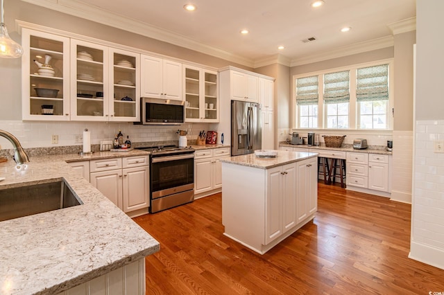 kitchen featuring stainless steel appliances, ornamental molding, white cabinetry, a sink, and wood finished floors