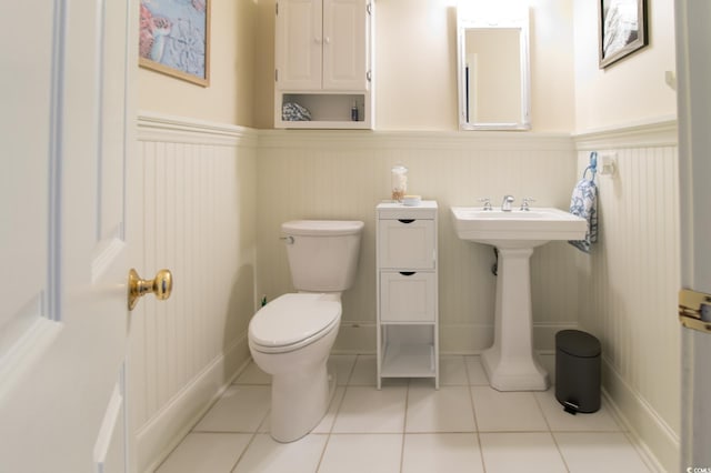 bathroom with toilet, wainscoting, a sink, and tile patterned floors