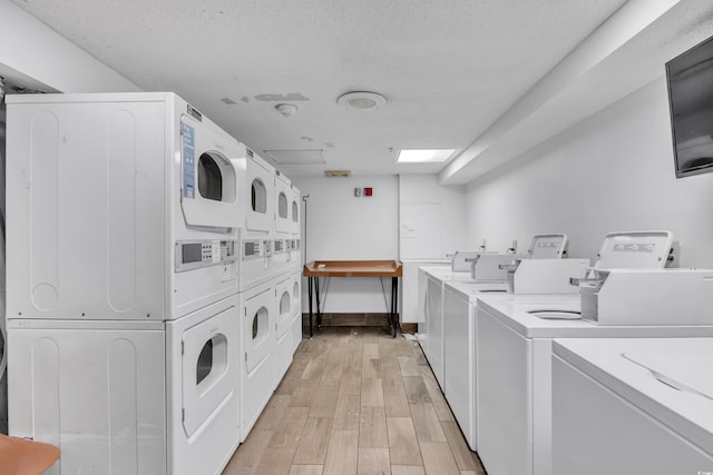 community laundry room with stacked washer and dryer, a textured ceiling, light wood-style flooring, baseboards, and washer and clothes dryer