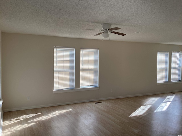 unfurnished room with a textured ceiling, wood finished floors, visible vents, and baseboards